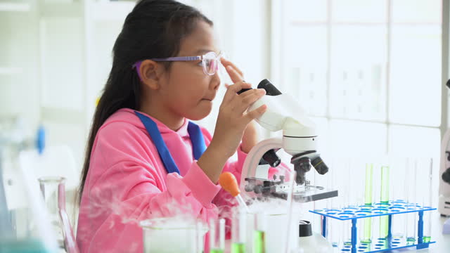 asian schoolgirl pupil student looking through microscope during science practical class in school laboratory. asia children scientists learning  biology chemistry lesson . Elementary School Science