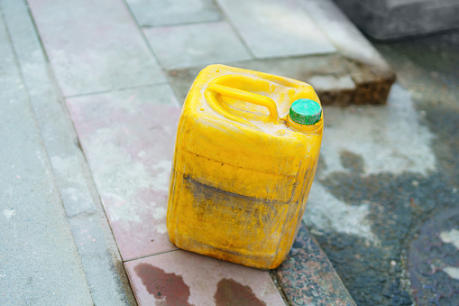 A yellow plastic liquid canister stands on the sidewalk