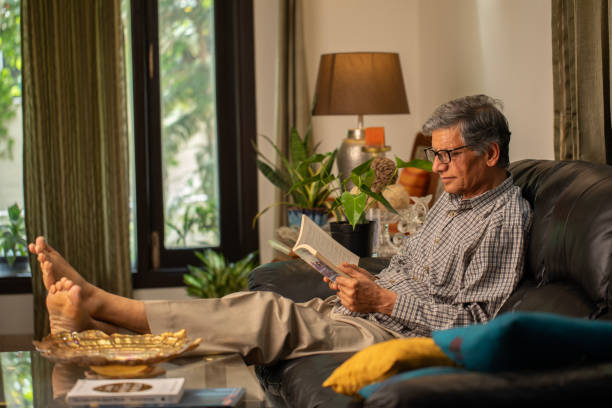 istock Senior man reading book on comfortable sofa at home 2148474351