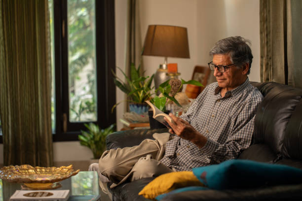 istock Senior man reading book on comfortable sofa at home 2148474371