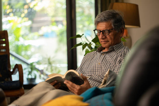 istock Senior man reading book on comfortable sofa at home 2148474398