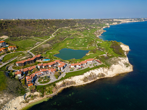 An overhead perspective of a golf course with lush greens near the ocean, showcasing sand traps and water hazards.