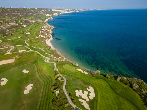 A birds-eye view of a lush green golf course situated near the ocean, with sand traps and water hazards visible.