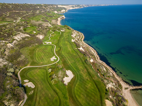 Aerial perspective of a golf course situated near the ocean, showcasing lush green fairways and sand traps.