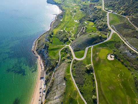 A birds eye view of a golf course located next to the ocean, showcasing the green fairways and sand traps against the backdrop of the sea.