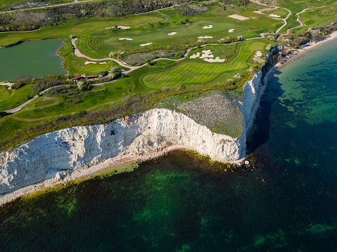 An overhead view of a golf course located near the ocean, showing green fairways, sand traps, and the blue ocean in the background.