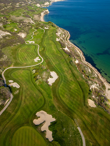 Aerial perspective of a golf course situated near the ocean, showcasing lush green fairways and sand traps.