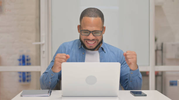 istock Excited Mixed Race Man Celebrating Success on Laptop 2148474583