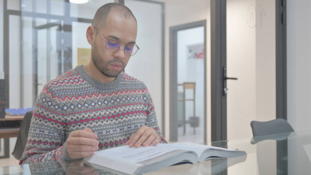 istock Young Hispanic Man Reading Book in Office 2148475336