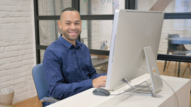 istock Hispanic Businessman Smiling at Camera while Working on Desktop in Office 2148476014