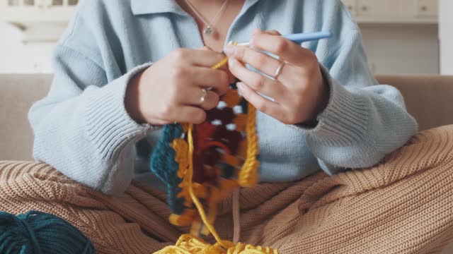 Young woman knitting crocheting with colored yarn granny square at home. Woman doing needlework, home hobbies