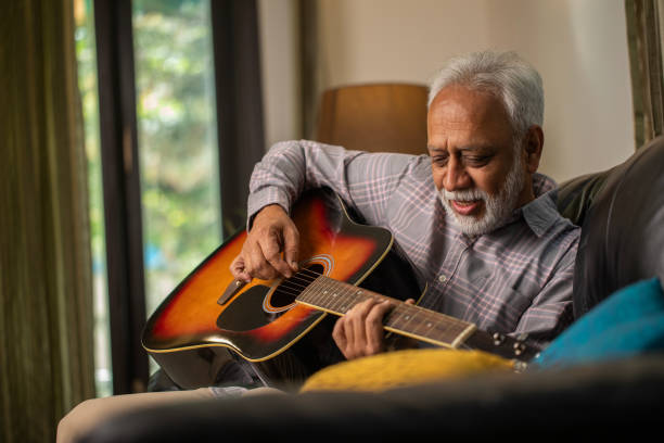 istock Old man looking away and playing guitar on sofa 2148476918