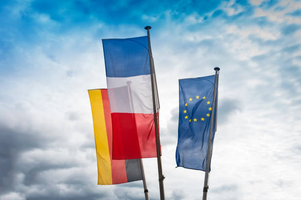 European French, German and EU flags side by side, waving in the wind against a dramatic cloudy sky