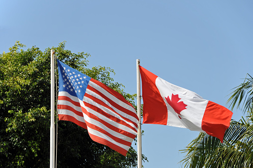 US and canadian flag side by side waving in the wind