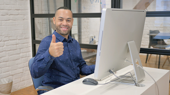 Thumbs Up by Hispanic Businessman while Working on Desktop