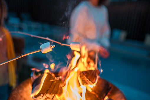 A person in casual attire roasts marshmallows over a blazing bonfire, engaging in a traditional outdoor activity.