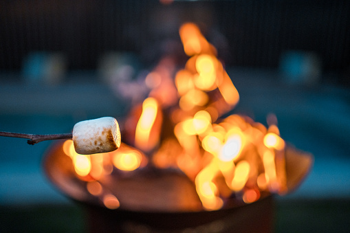 An outdoor evening scene where an individual roasts a marshmallow over a glowing fire, highlighting a popular leisure activity and the use of simple roasting tools.