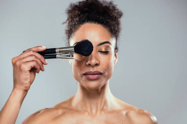 istock Beautiful young woman making make-up while looking at camera in isolated white 2148479421