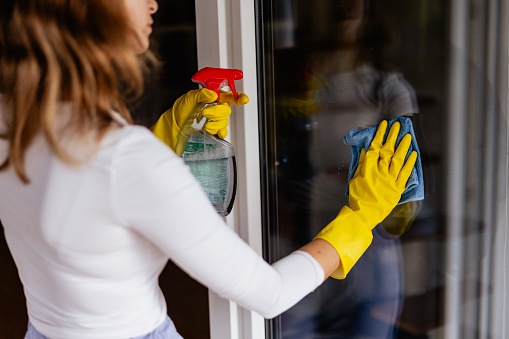 Young woman washing window at home, spring cleaning concept