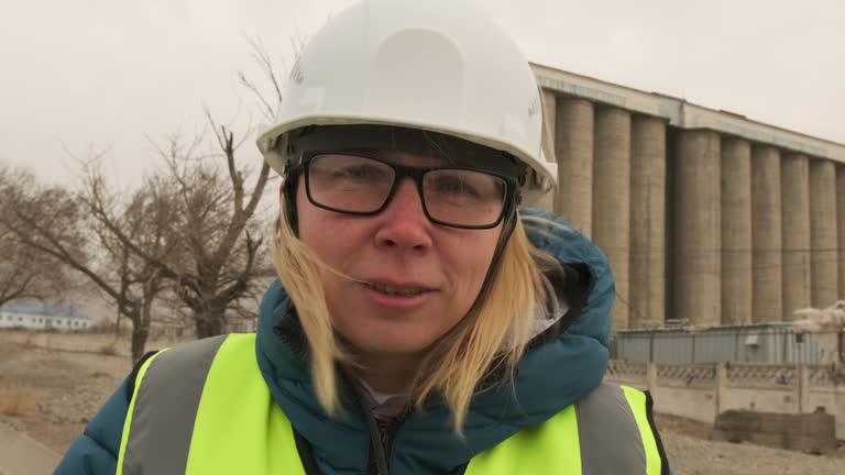 Young female construction worker in hardhat smiling on building background.