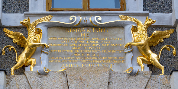 Two gilded guardian griffon statues standing beside baroque dedication plaque from 1672 on historical facade in Eisenstadt, Burgenland, Austria