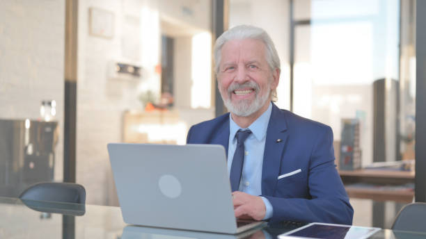 istock Old Businessman Smiling at Camera while Working in Office 2148489235