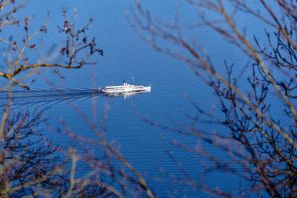 Aerial view of white paddle steamer Uri with waving Swiss flag crossing Swiss Lake Lucerne on a sunny spring day. Photo taken April 11th, 2024, Bürgenstock, Lake Lucerne, Switzerland.