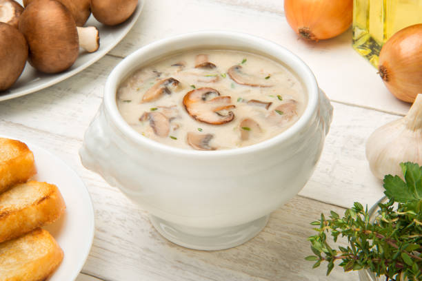 Cream of mushroom soup in a white porcelain tureen on a white rustic table with ingredients. Selected focus. stock photo