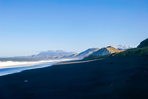 A long beach stretches into the distance with snow capped mountains on the west coast of New Zealand
