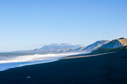 A long beach stretches into the distance with snow capped mountains on the west coast of New Zealand