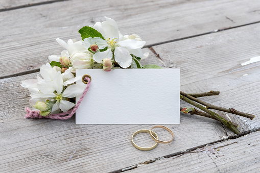 Apple blossom branches and card with copy space and golden rings on a wooden background