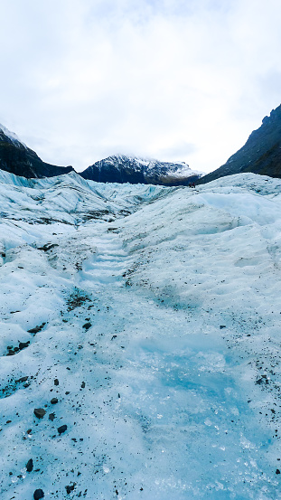 A glacier nestled among a mountainous valley on an overcast day showing blue hues of light and air trapped in the slow moving ice