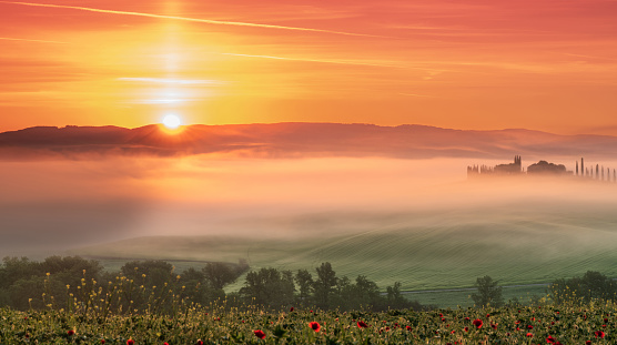 Pienza, Tuscany, Italy  April 13, 2024: House surrounded by cypress trees among the misty morning sun-drenched hills of the Val d'Orcia valley at sunrise in San Quirico d'Orcia, Tuscany, Italy