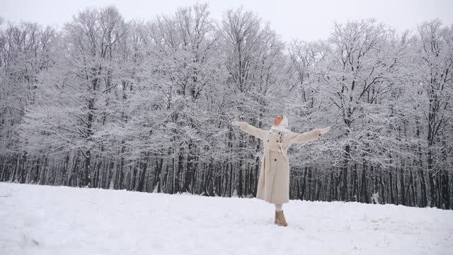 Woman in white scarf and coat standing in snowy forest. Lady standing in snow-covered woods. Winter scene with woman in white coat walking in the winter forest. Female in snowy forest landscape. Snowy forest backdrop with woman in white coat.