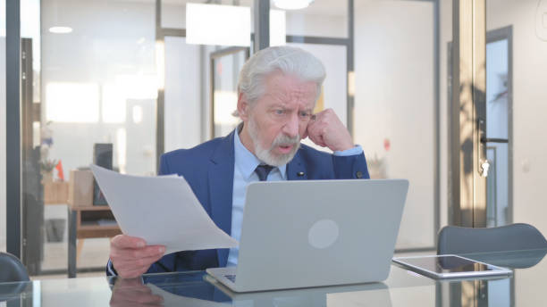 istock Senior Businessman Feeling Upset while Reading Contract and Using Laptop 2148496266