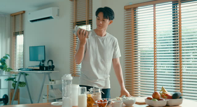Young Asian man preparing protein shake at modern home. Diet and healthy food morning routine.