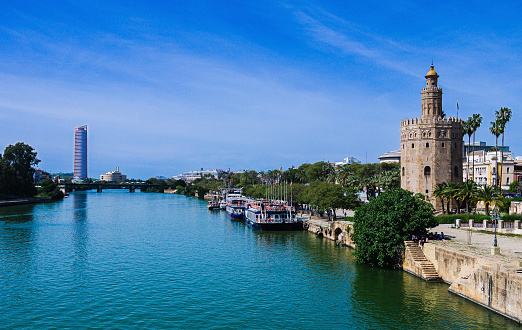 sevilla, spain-april 4, 2024: views of the guadalquivir river as it passes through sevilla, next to the torre del oro and in the background the selvilla tower, copy space.