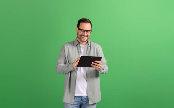 istock Smiling young businessman in eyeglasses reading e-mails over digital tablet on green background 2148497770