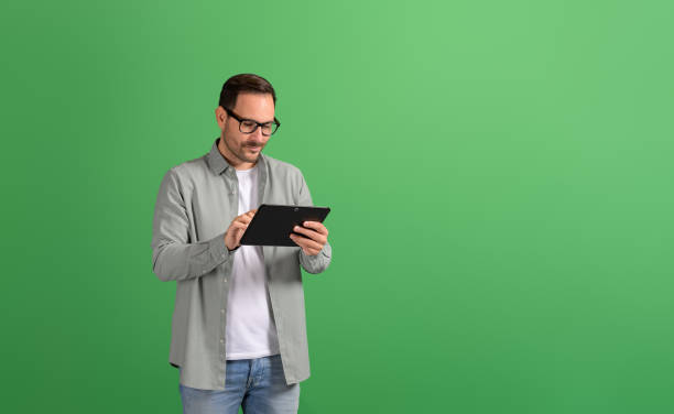 istock Focused young businessman doing online research over digital tablet on isolated green background 2148497771
