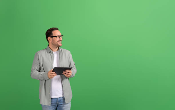 istock Successful businessman with digital tablet smiling and looking away thoughtfully on green background 2148497787