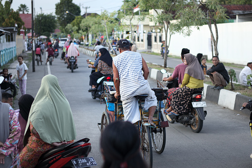 Cilacap, Indonesia - April 12, 2024 : a pedicab driver taking his passengers to their desired destination amidst a crowd of people in the middle of the road