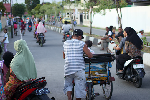 Cilacap, Indonesia - March 29, 2024 : a pedicab driver taking his passengers to their desired destination amidst a crowd of people in the middle of the road