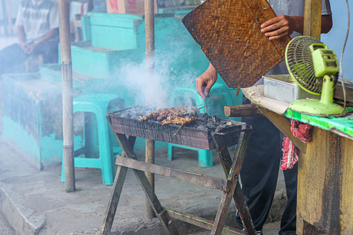 Cilacap, Indonesia - March 29, 2024 : activity of a chicken satay seller who is grilling chicken meat ordered by his buyer at a small food stall on the side of the main road