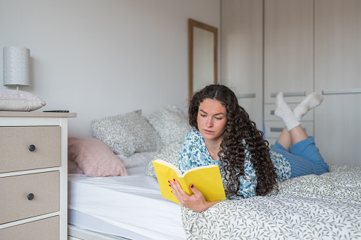 Woman engrossed reading a book at home on the bed in the daytime