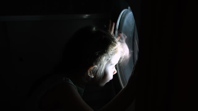 A little girl plays near the washing machine door, imagining that she is in space.