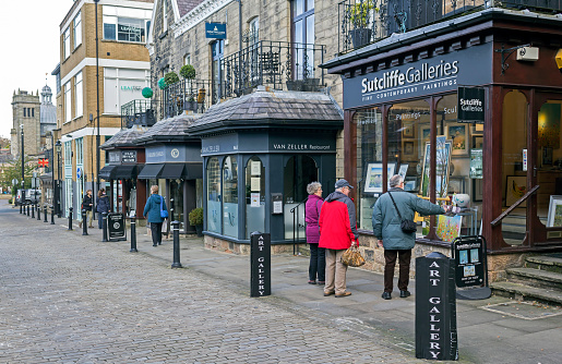 View along a street in the centre of York, UK.  People can be seen looking into shop windows and walking on the pavements.