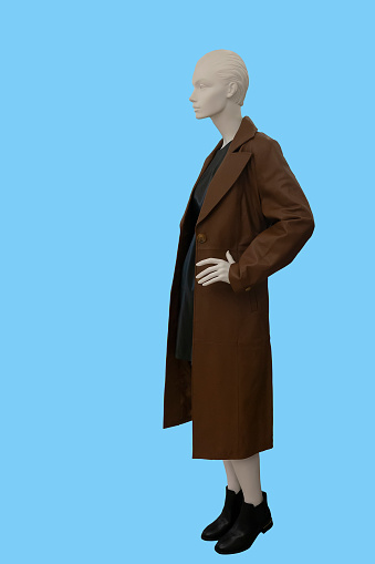 Full length image of a female display mannequin dressed in brown demi-season overcoat isolated on blue background