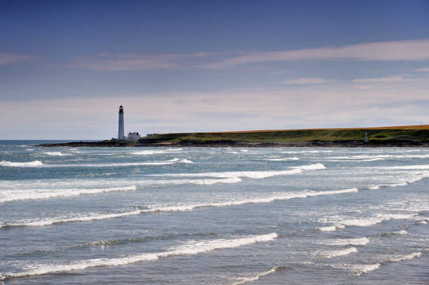 A bright and jolly day with the sunlight glistening off the sea as the waves rolling in across Montrose Beach with Scurdie Ness lighthouse standing guard across the bay.