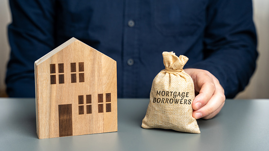 Mortgage borrowers concept. Individuals or entities who have taken out a mortgage loan from a lender to finance the purchase of a property. Money bag and miniature house