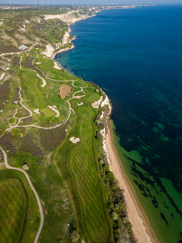 An aerial perspective of a golf course situated near the ocean, showcasing the lush green fairways and sand bunkers against the backdrop of the sea.